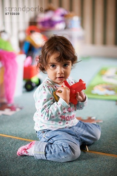 Kleinkind auf dem Spielzimmerboden sitzend mit rotem Spielzeug spielend