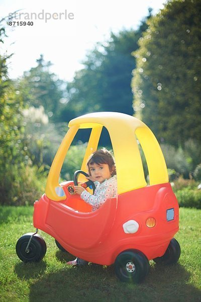 Kleinkind beim Spielen im Spielzeugauto im Garten