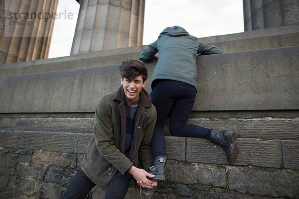 Ein junger Mann hilft seiner Freundin auf das National Monument am Calton Hill in Edinburgh  Schottland.