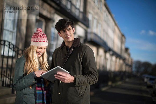 Ein junges Paar spaziert auf der Regent Terrace in Edinburgh  Schottland und schaut sich seinen Tablet-Computer an.