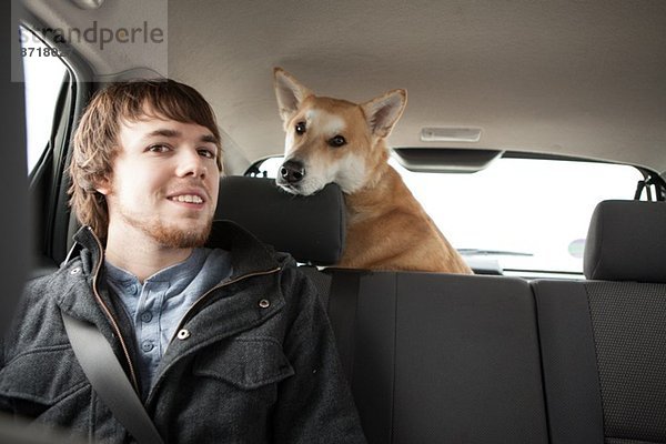 Junger Mann und sein gekreuzter Schäferhund im Autositz