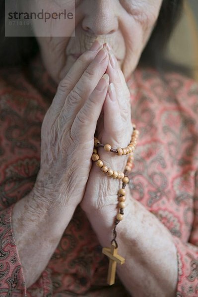Seniorin betend mit Rosenkranz