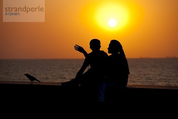 sitzend  Sonnenuntergang  jung  zeigen  Uferdamm  Bombay  Indien  indische Abstammung  Inder