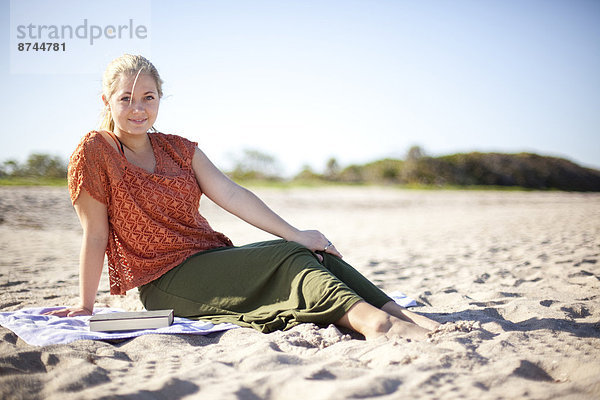 Vereinigte Staaten von Amerika USA sitzend Portrait Frau sehen Buch Strand Blick in die Kamera jung Taschenbuch