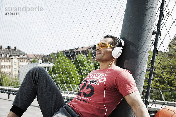 sitzend  Mann  zuhören  Kopfhörer  Musik  reifer Erwachsene  reife Erwachsene  Basketball  Kleidung  Außenaufnahme  Gericht  Deutschland