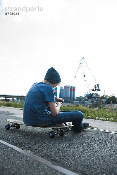 Außenaufnahme  sitzend  sehen  Junge - Person  Industrie  Telefon  Skateboard  Zimmer  Rückansicht  Handy  Deutschland  freie Natur