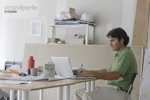 Männlich Architekt mit Laptop auf behelfsmäßigen Schreibtisch in Website-Büro