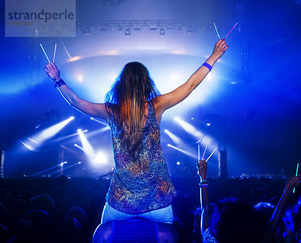 Jubelnde Frau mit Leuchtstäben auf den Schultern des Mannes beim Musikfestival