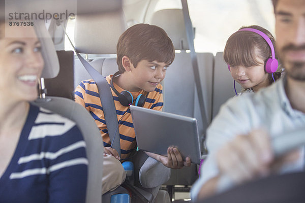 Bruder und Schwester teilen sich ein digitales Tablett auf dem Rücksitz des Autos.