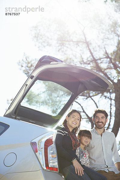 Porträt einer lächelnden Familie  die am Heck des Autos sitzt.