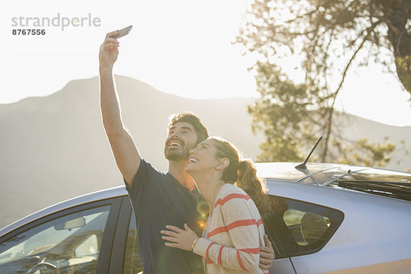 Glückliches Paar beim Selbstporträt mit Fotohandy außerhalb des Autos