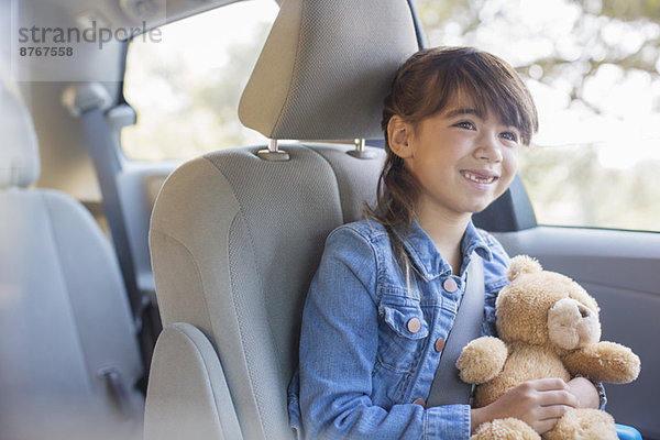 Glückliches Mädchen mit Teddybär auf dem Rücksitz des Autos