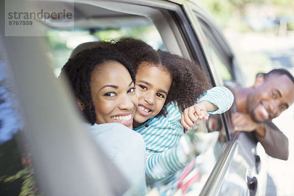 Porträt einer glücklichen Familie  die sich aus den Autoscheiben lehnt.