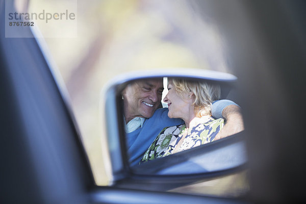 Seitenspiegelreflexion der Paarumarmung im Auto