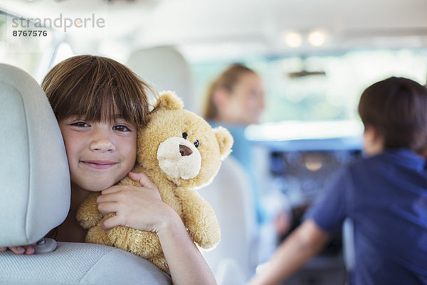 Porträt des glücklichen Mädchens mit Teddybär auf dem Rücksitz des Autos