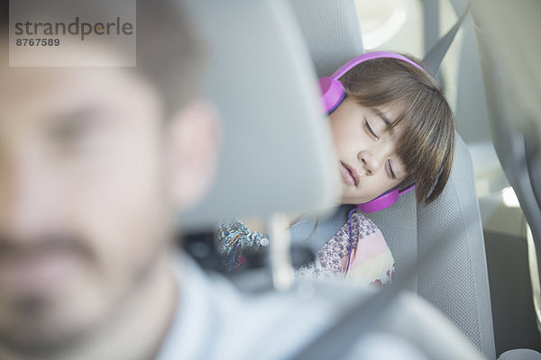Mädchen mit Kopfhörer  das auf dem Rücksitz des Autos schläft