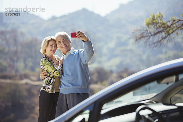 Seniorenpaar beim Selbstporträt mit Handy vor dem Auto