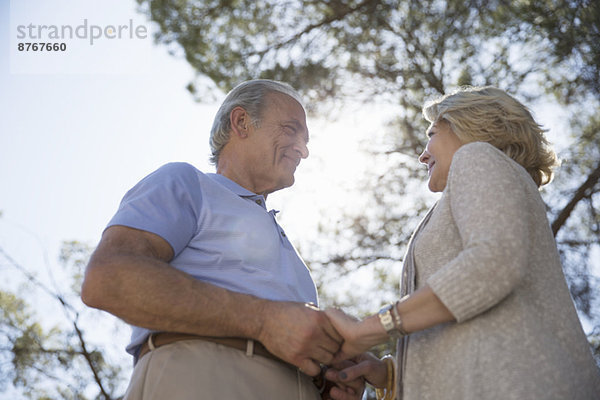 Glückliches älteres Paar hält sich an den Händen unter dem Baum