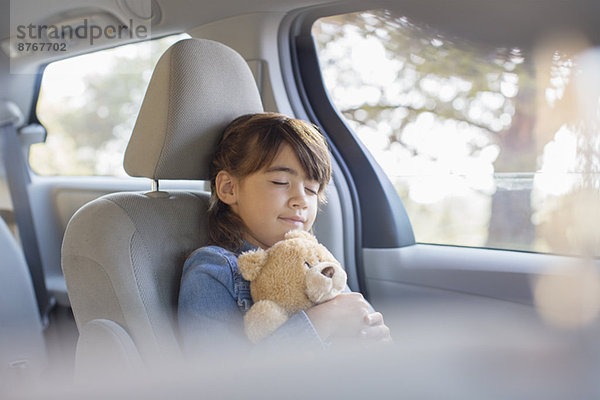 Mädchen mit Teddybär schläft auf dem Rücksitz des Autos