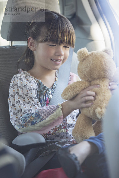Mädchen mit Teddybär auf dem Rücksitz des Autos
