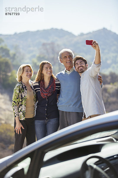 Selbstporträt der Familie mit Handy außerhalb des Autos