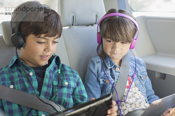 Bruder und Schwester mit Kopfhörer mit digitalen Tabletts auf dem Rücksitz des Autos