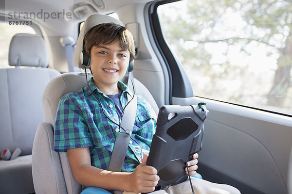 Porträt eines glücklichen Jungen mit Kopfhörer mit digitalem Tablett auf dem Rücksitz des Autos