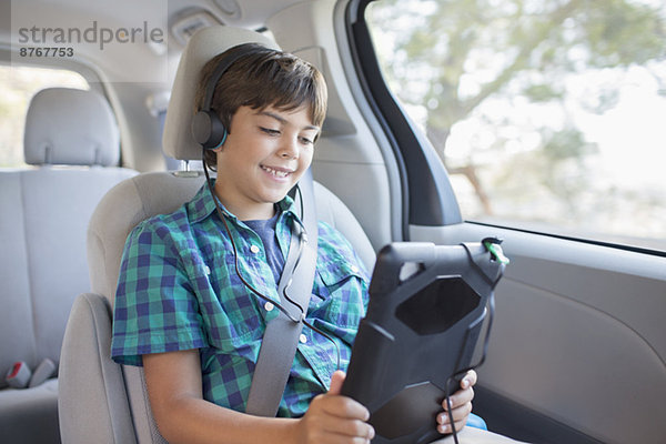 Glücklicher Junge mit digitalem Tablett auf dem Rücksitz des Autos