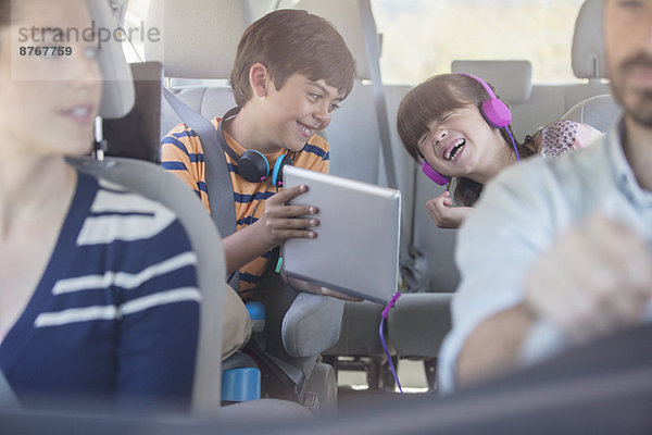 Glückliche Geschwister mit digitalem Tablett auf dem Rücksitz des Autos