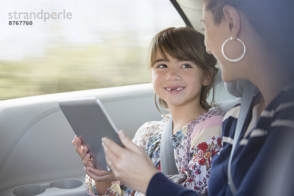 Glückliche Mutter und Tochter mit digitalem Tablett auf dem Rücksitz des Autos