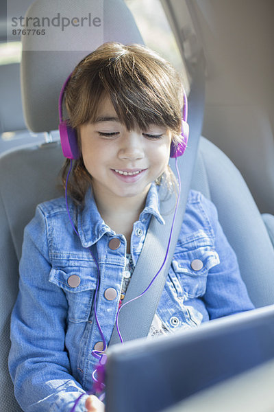 Glückliches Mädchen mit Kopfhörer mit digitalem Tablett im Auto