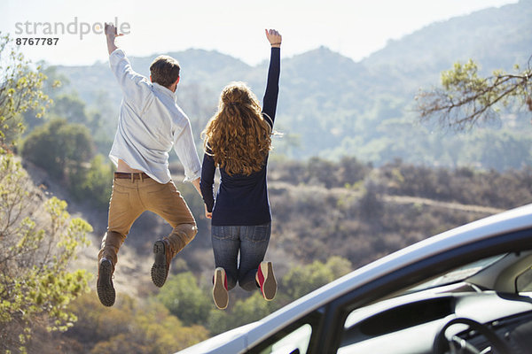 Enthusiastisches Paar  das vor Freude außerhalb des Autos springt.
