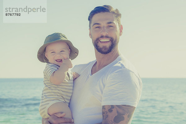 Porträt von Vater und Sohn lächelnd am sonnigen Strand