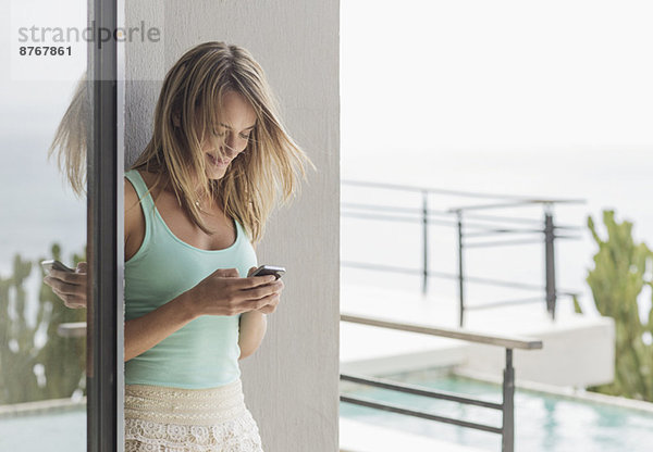 Lächelnde Frau SMS mit Handy auf der Terrasse