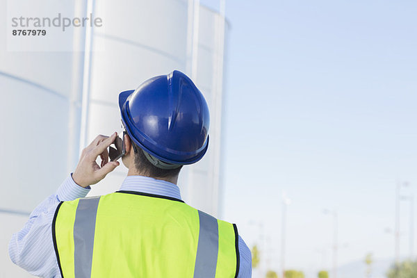 Arbeiter spricht am Handy und schaut zu den Silo-Lagertürmen hinauf