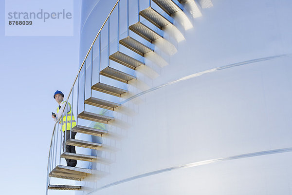 Arbeiter mit Walkie-Talkie auf einer Treppe  die sich am Silo-Lagerturm entlang schlängelt.