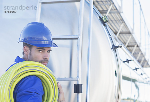 Porträt eines seriösen Arbeiters mit Schlauch an der Rückseite des Edelstahltankers