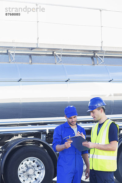 Arbeiter mit Klemmbrett reden neben dem Edelstahltankwagen