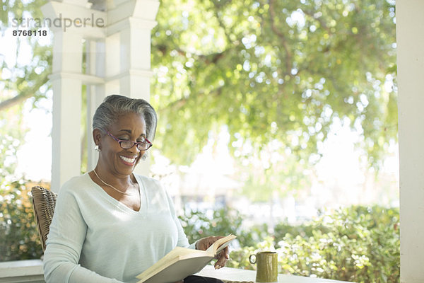 Glückliche Seniorin beim Lesen auf der Veranda