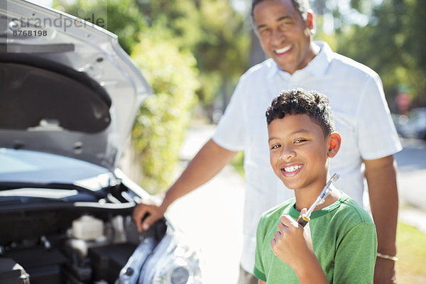 Porträt eines lächelnden Enkels  der den Motor eines Autos mit Großvater repariert