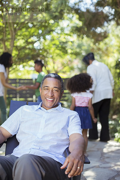 Porträt eines lächelnden älteren Mannes auf der Terrasse mit Familie im Hintergrund