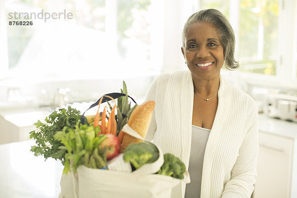 Porträt der lächelnden Seniorin mit Lebensmitteln in der Küche