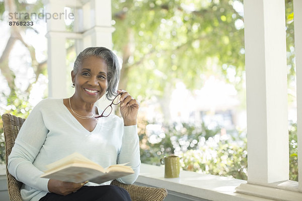 Porträt der lächelnden Seniorin beim Lesen auf der Veranda