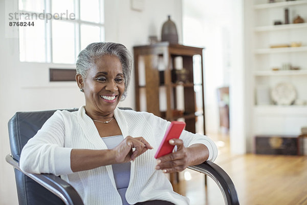 Glückliche Seniorin SMS mit Handy im Wohnzimmer