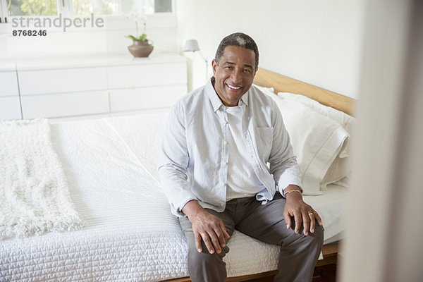 Porträt eines lächelnden älteren Mannes auf dem Bett sitzend