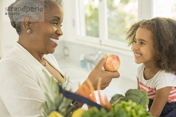 Glückliche Großmutter schenkt Enkelin Apfel in der Küche