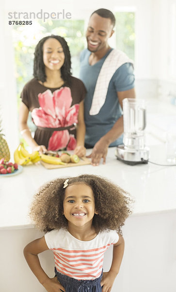 Porträt eines begeisterten Mädchens in der Küche mit Eltern im Hintergrund