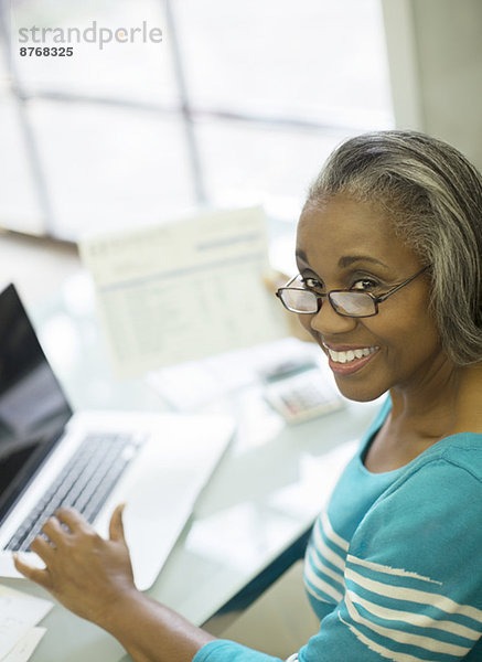 Porträt einer lächelnden Seniorin  die Rechnungen am Laptop zahlt
