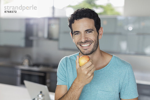 Porträt eines lächelnden Mannes beim Apfelessen in der Küche