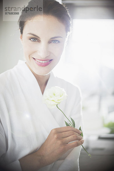 Porträt der lächelnden Frau im Bademantel mit weißer Rose